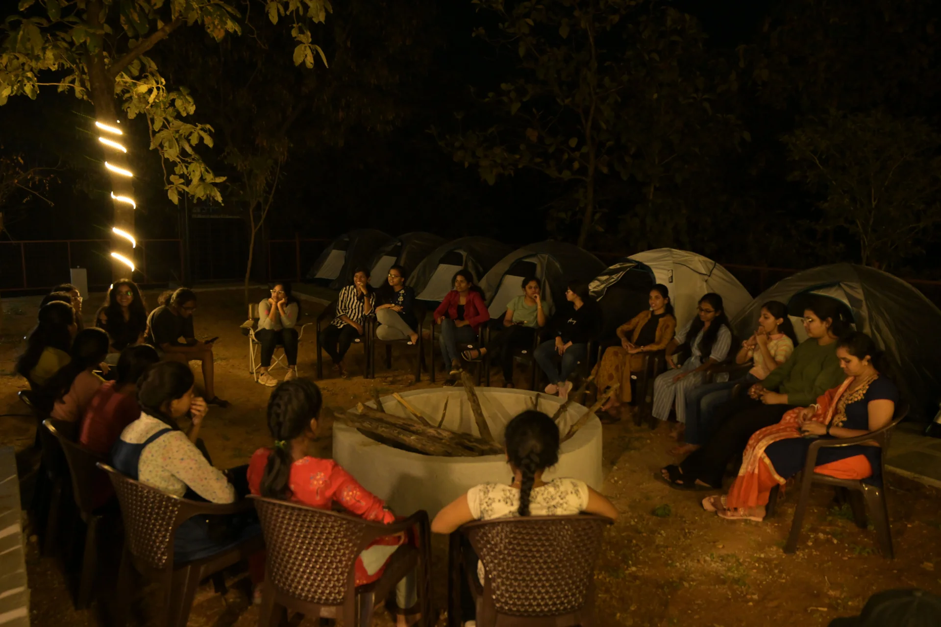 Group around a firepit with tents at night on Village Trails camp