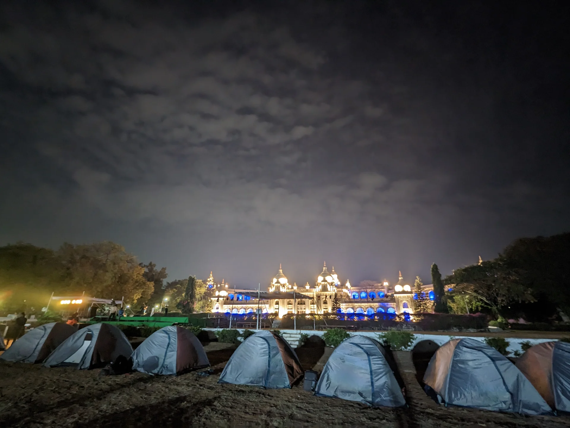 Student tents pitched at night with the illuminated Mysore Palace behind - a classic school trip destination